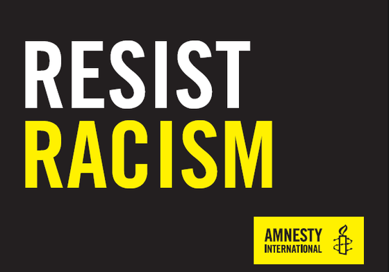 A black placard that reads 'Resist Racism' with an Amnesty logo in the bottom-right corner