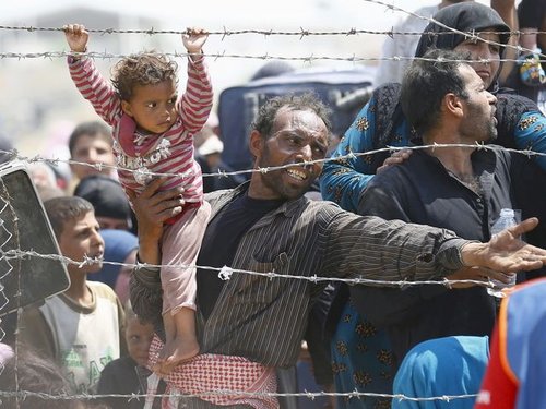 A Syrian refugee reacts as he waits behind border fences to cross into Turkey at