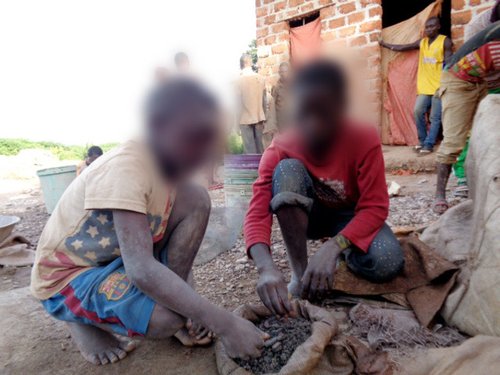 Two young children crouch and sort through rocks to find cobalt, a key metal used in the manufacture of car batteries