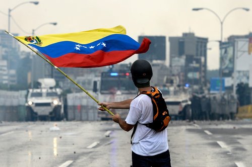 A Venezuelan opposition demonstrator waves a flag at the riot police