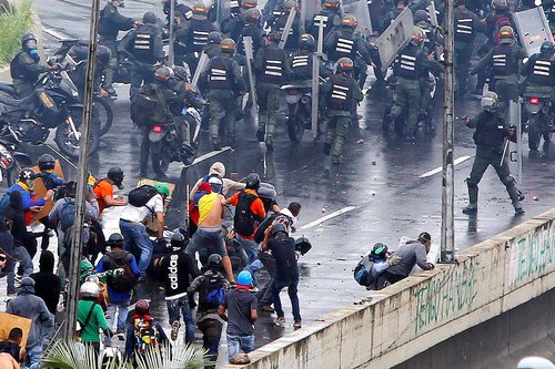 A member of the riot security forces points a gun towards a crowd of demonstrators in Venezuela