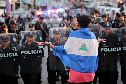 An anti-government protester wearing a national flag shouts slogans in front of a line of riot police during a protest against Nicaraguan President Ortega's government in Managua