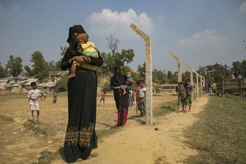 Rohingya refugees walk near a fence that is being constructed around the refugee camp on December 11, 2019
