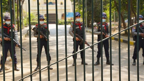 Picture of five armed policemen standing in a line behind a gate during a protest in Myanmar in February