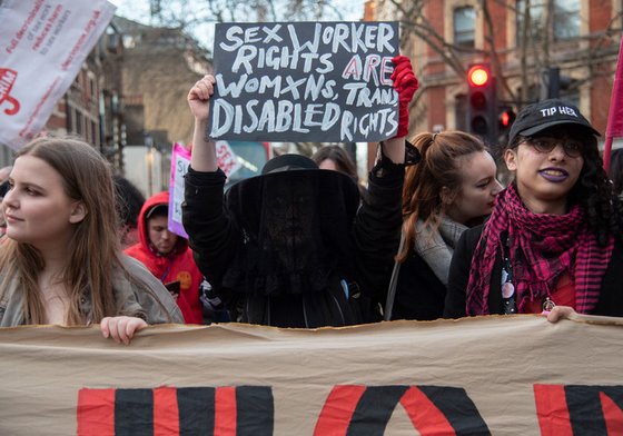 Three women march at a demonstration, with the central figure holding a placard saying 'Sex worker rights are women's rights, trans rights and disabled rights'