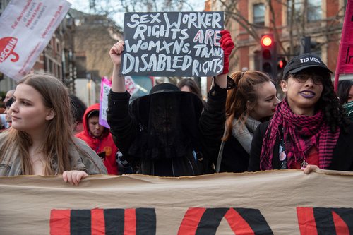 Three women march at a demonstration, with the central figure holding a placard saying 'Sex worker rights are women's rights, trans rights and disabled rights'