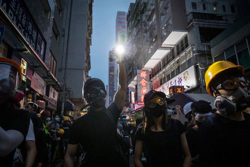 Anti-government protesters wearing gas masks and holding placards march on Hong Kong at dusk