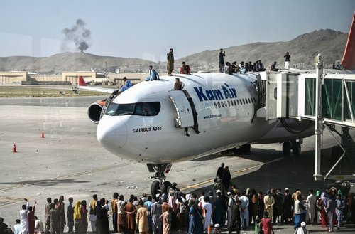 Afghan people climb on top of a plane as they wait at the Kabul airport in Kabul on August 16, 2021