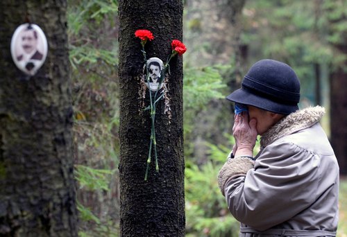 A woman reacts next to a portrait of a victim of Soviet dictator Joseph Stalin's purges at the memorial, where the victims were buried in the woods on the outskirts of Saint-Petersburg, on October 30, 2017.