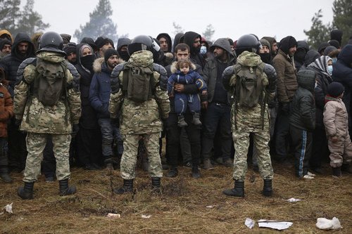 Migrants stand in front of Belarusian servicemen as they gather in a camp near the Belarusian-Polish border in the Grodno region on November 14 2021
