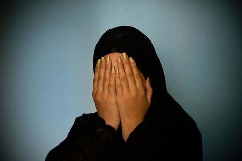 Woman in hijab holds her head in her hands with painted nails