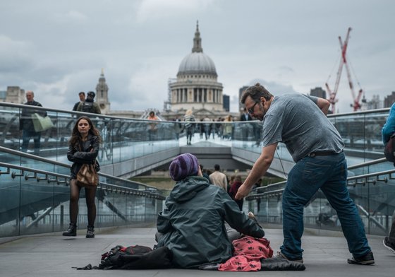 Someone donating to a homeless person sitting near the Millennium bridge in London