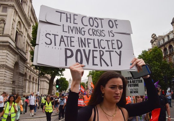 Woman at UK protest holds placards saying 'The Cost of Living Crisis is State Inflicted Poverty'