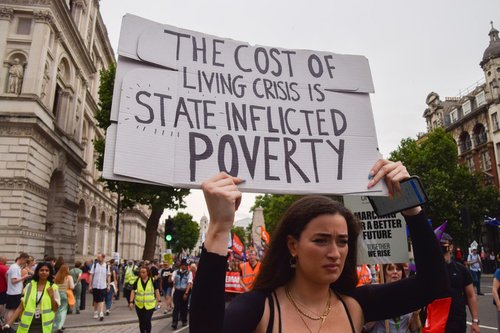 Woman at UK protest holds placards saying 'The Cost of Living Crisis is State Inflicted Poverty'