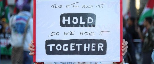Placard saying 'this is too much to hold, so we hold it together'
