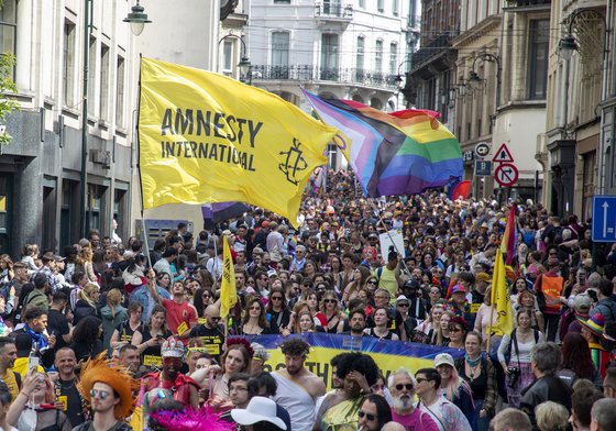A sea of Amnesty protestors waving an Amnesty and a Progress Pride flag in a street.