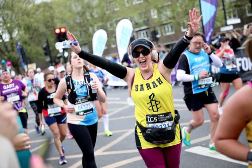 Amnesty London marathon runner smiling with hands in the air while runners for other charities run in the background
