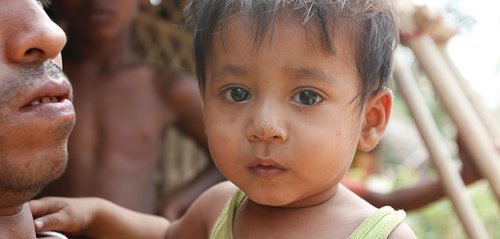 Rohingya man holding a child who is looking at the camera