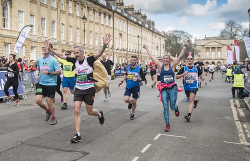 Image shows people running through bath with their arms raised and smiling.