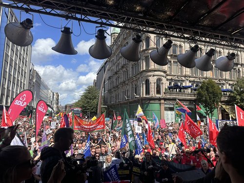 Colourful view from the stage of thousands of people - many holding aloft banners, flags and placards - gathered in front of Belfast City Hall to rally against racism.