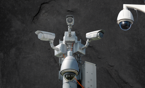On a dark grey background, there are cut out images of 5 CCTV cameras to evoke the surveillance this community are under