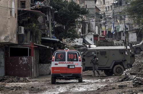 An ambulance trying to cross an army blockage in Gaza in a street with lots of rubble.