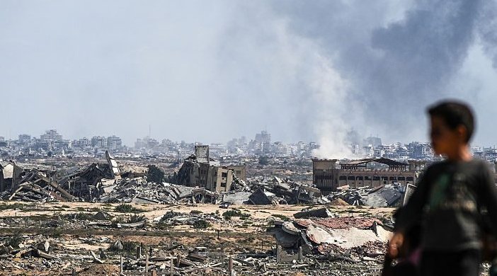 A young boy stands in the foreground looking into the distance - a scene of massive destruction in Gaza
