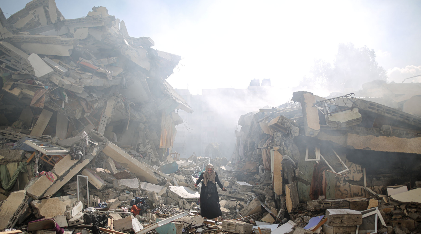 A Palestinian woman stands among complete devastation of street with buildings turned to rubble.