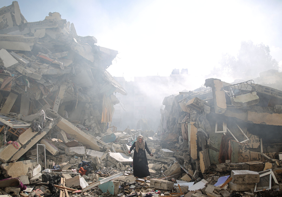 A Palestinian woman stands among complete devastation of street with buildings turned to rubble.
