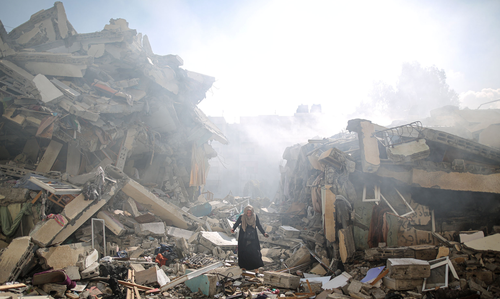 A Palestinian woman stands among complete devastation of street with buildings turned to rubble.