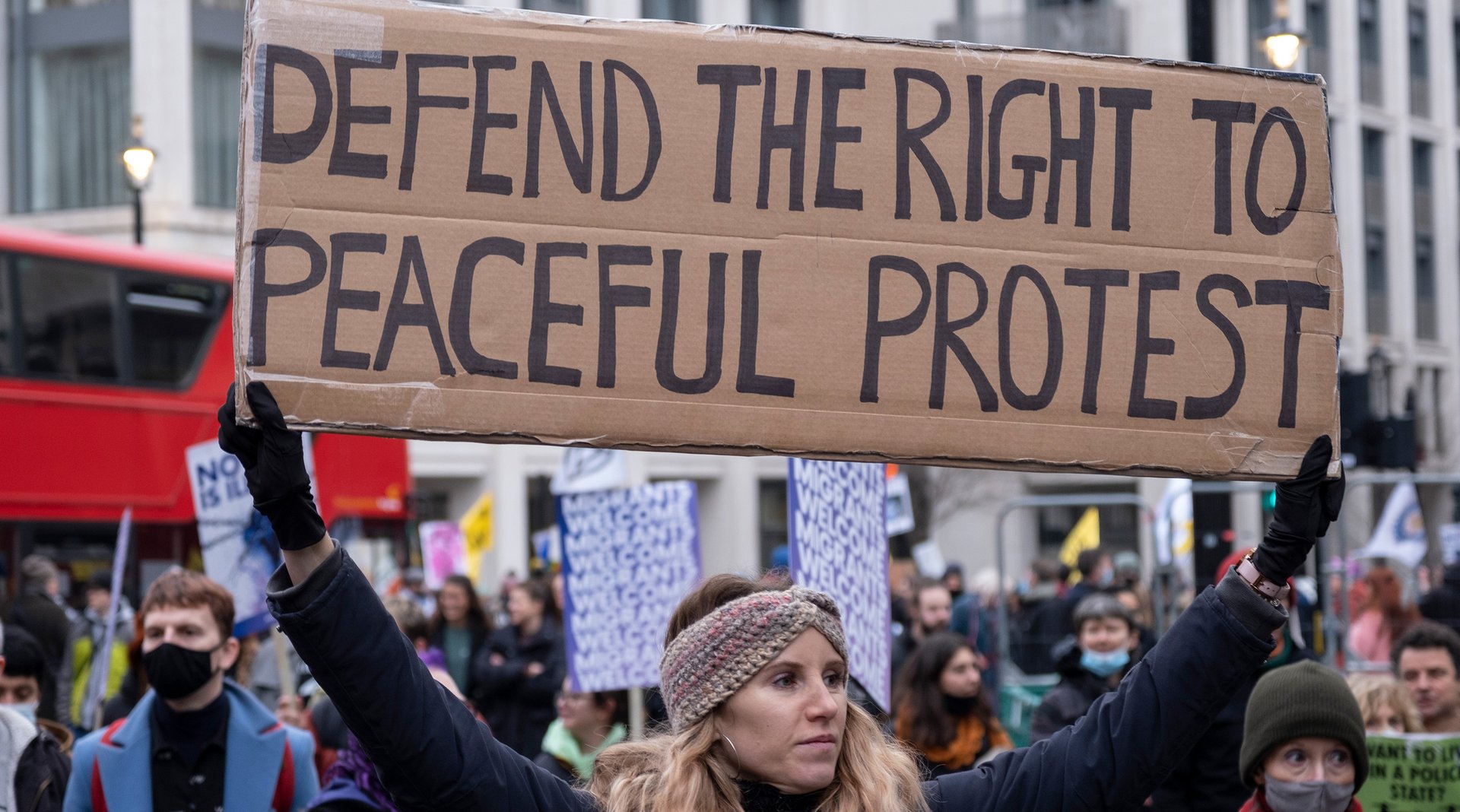 A woman holding up a placard saying 'Defend the right to peaceful protest'