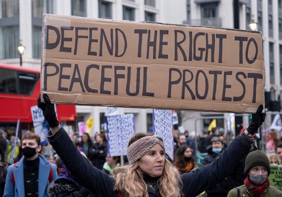 A woman holding up a placard saying 'Defend the right to peaceful protest'