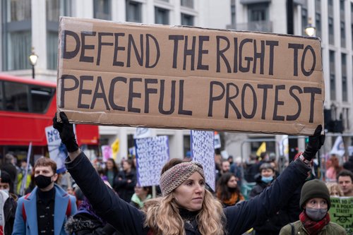 A woman holding up a placard saying 'Defend the right to peaceful protest'