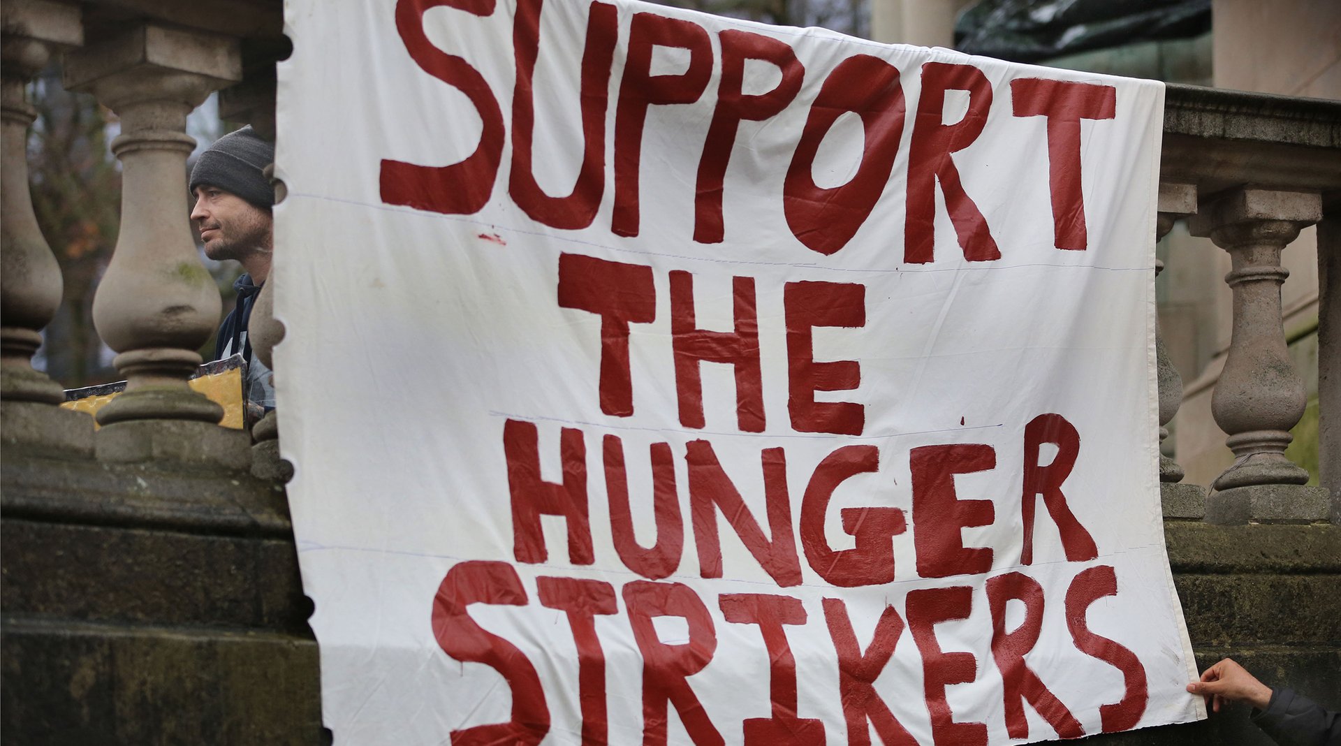 Photograph of a large homemade white banner with red writing on saying 'SUPPORT THE HUNGER STRIKERS'