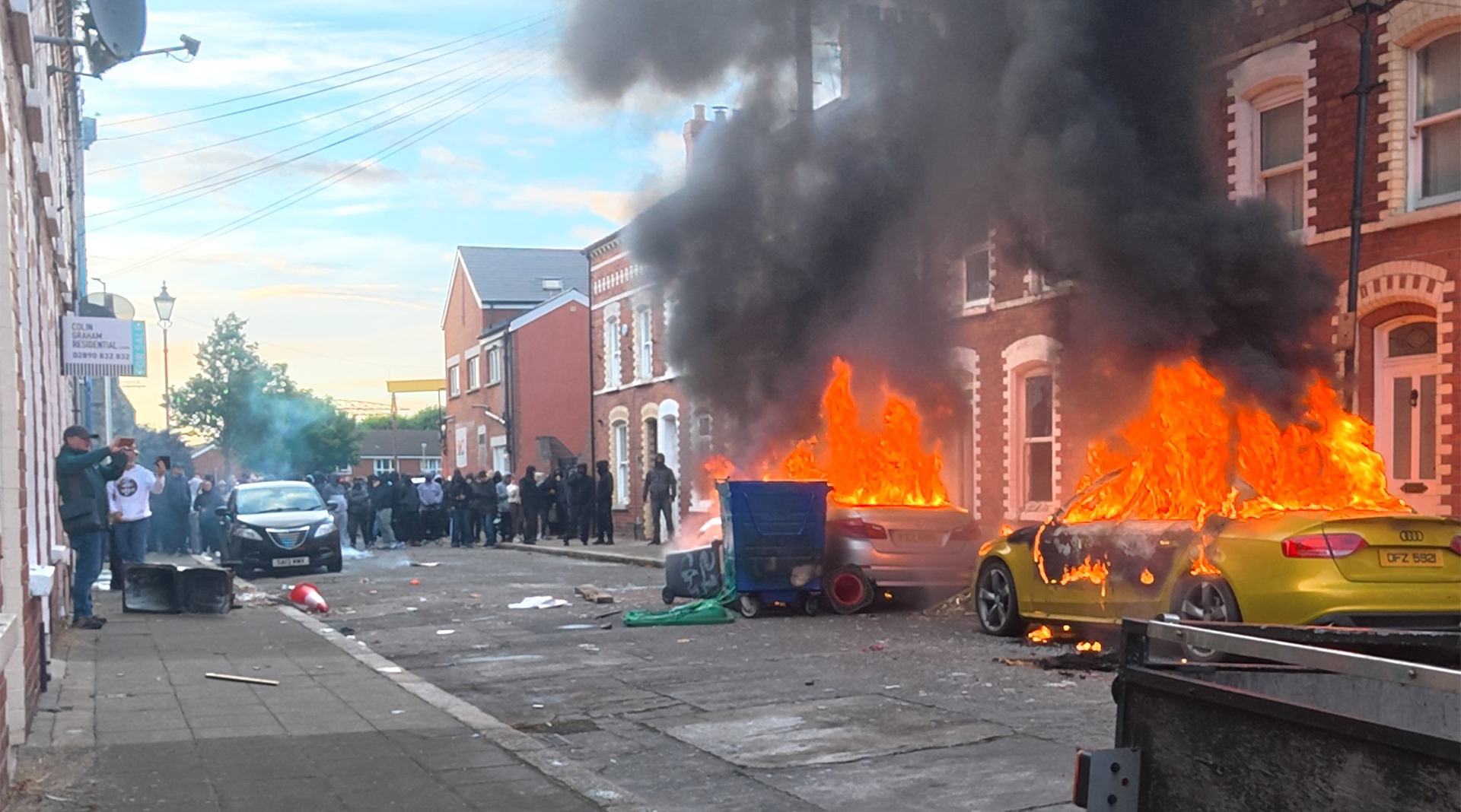 Flames and thick black smoke rise from a vehicle on a terraced street during racist riots in Belfast, Northern Ireland, June, 2026
