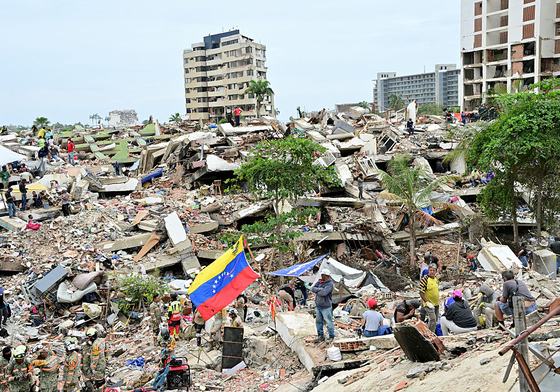 Members of a Mexican Army rescue unit and volunteers work amid the rubble of collapsed buildings as a Venezuelan flag stands in Caraballeda, La Guaira state, Venezuela, on July 3, 2026. The death toll from Venezuela's twin earthquakes has risen to 2,595.