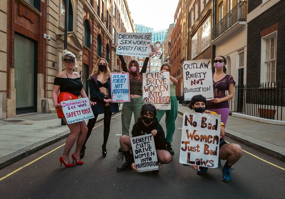 A group of women standing in the street while holding signs about decriminalising sex work, and its relationship with benefit cuts