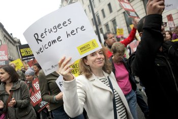 Woman holding sign saying Refugees Welcome here at a protest