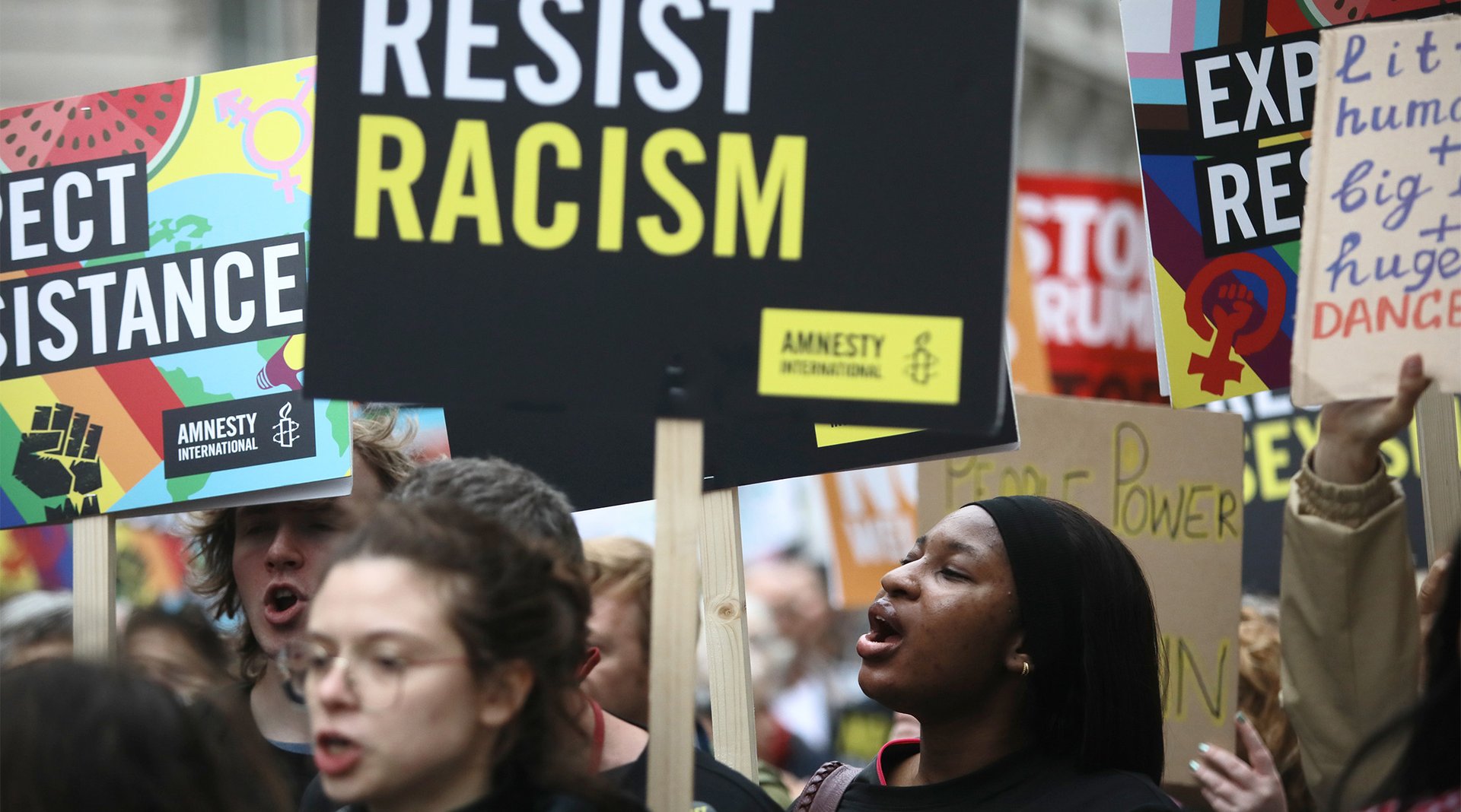 Protesters on a busy march hold up a placard that says 'RESIST RACISM'