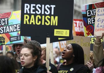Protesters on a busy march hold up a placard that says 'RESIST RACISM'