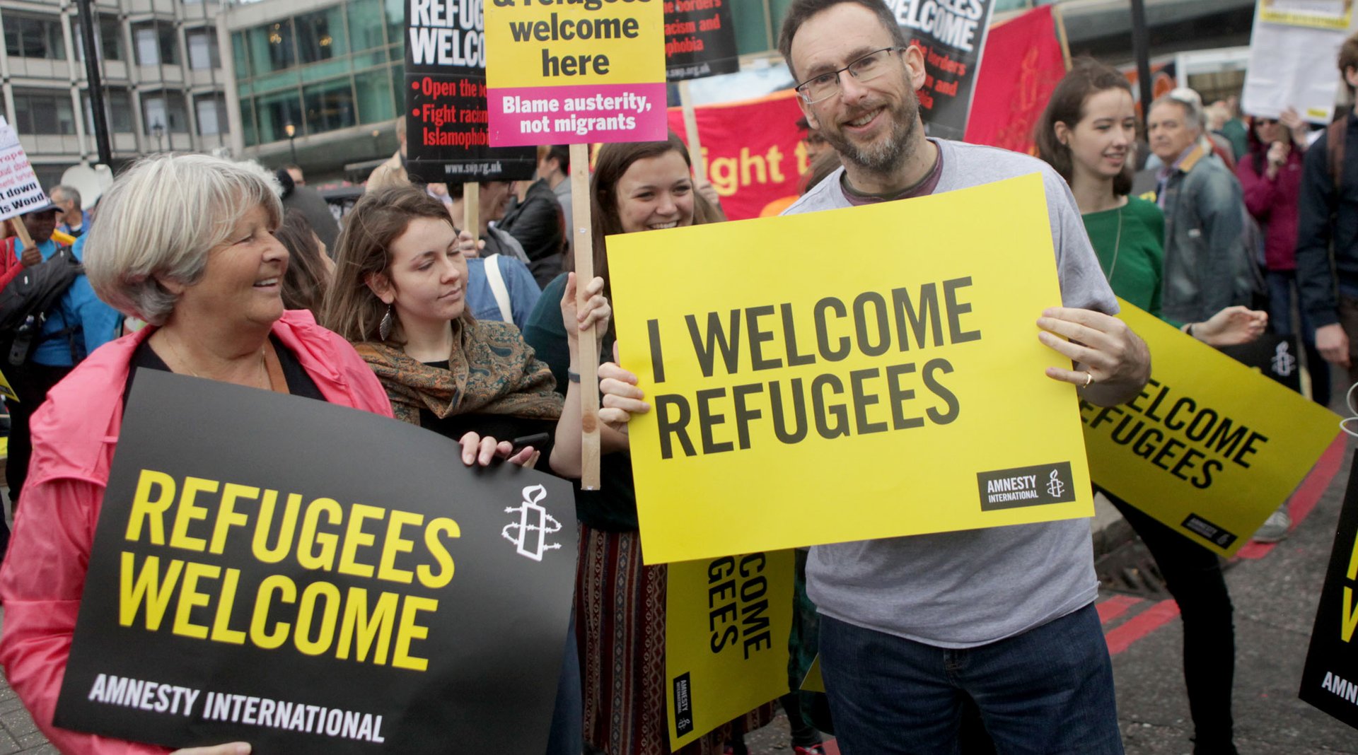 Woman holding sign saying Refugees Welcome here at a protest
