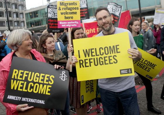 Woman holding sign saying Refugees Welcome here at a protest