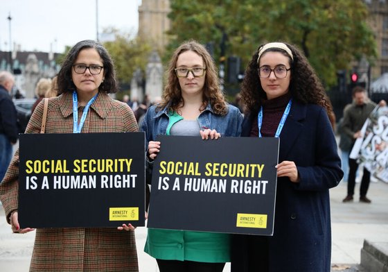 Three people hold up a sign saying "social security is a human right" in front of Westminster, London