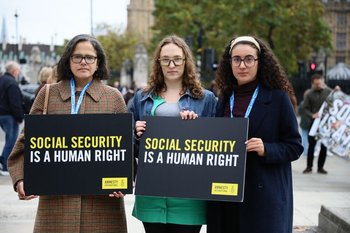 Three people hold up a sign saying "social security is a human right" in front of Westminster, London