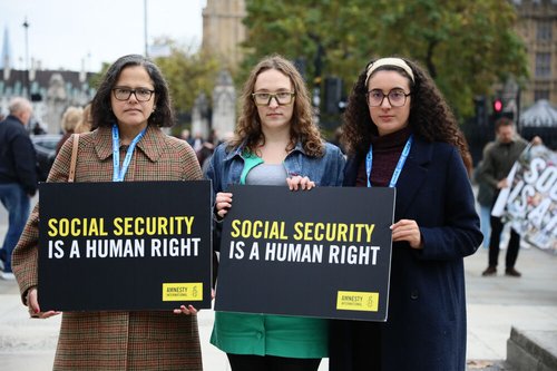 Three people hold up a sign saying "social security is a human right" in front of Westminster, London