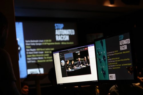 Photograph showing a laptop screen with large screens in the background saying 'Stop automated racism'