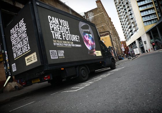 Truck parked on a road with a banner on all sides promoting Amnesty's predictive policing campaign.