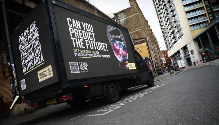 Truck parked on a road with a banner on all sides promoting Amnesty's predictive policing campaign.