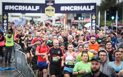 Image shows people running in front of an arch for he Manchester half marathon
