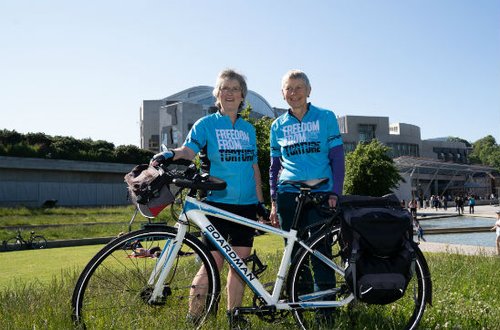 Image shows two women and a bicycle outside the Scottish Parliament